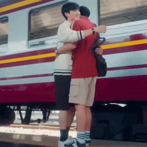 two young men hugging each other in front of a train .