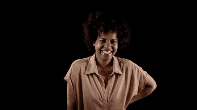 a woman in a brown shirt smiles with her hand on her hip