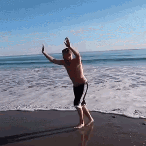 a man dancing on the beach with his arms outstretched