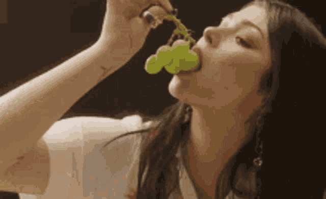 a woman is eating a bunch of grapes with a tattoo on her arm