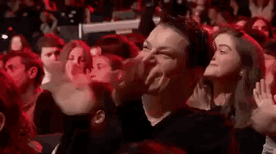 a man is laughing in a crowd of people at a concert while a woman looks on .