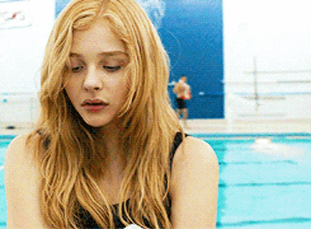 a woman in a black tank top is standing in front of a swimming pool with her eyes closed