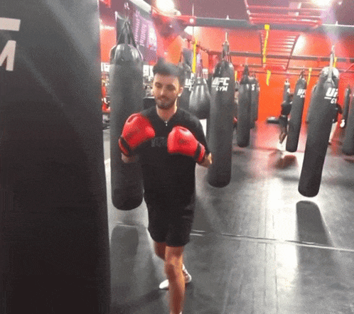 a man wearing red boxing gloves is in a gym with ufc bags
