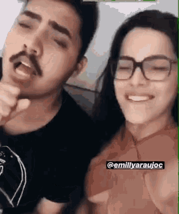a man with a mustache and glasses is singing into a microphone next to a woman with glasses .