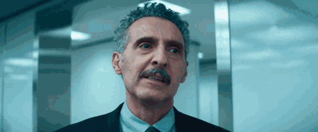 a man with curly hair and a mustache is wearing a suit and tie
