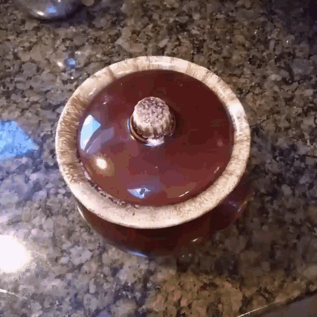 a red bowl with a wooden handle sits on a granite counter