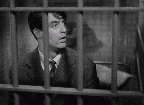 a man in a suit and tie is looking out of a jail cell .
