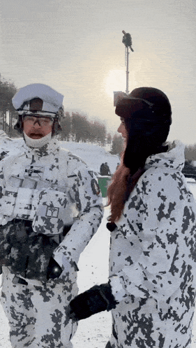 a man and a woman are standing in the snow and the man is wearing a camouflage jacket