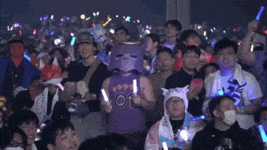 a crowd of people holding glow in the dark sticks with one man wearing a mask that says ' oh ' on it