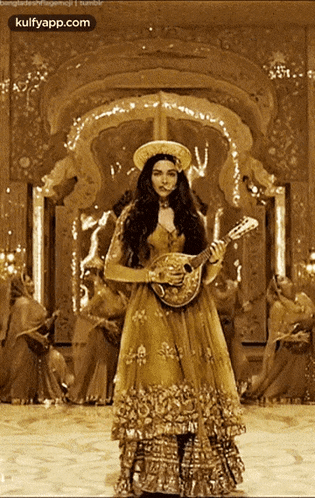 a woman in a gold dress is holding a guitar in front of a crowd of people