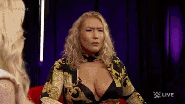 a woman in a very revealing top is sitting on a red chair talking to another woman .