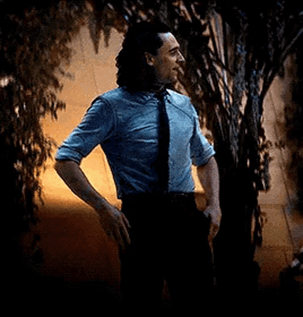 a man in a suit and tie is standing in front of a tree .