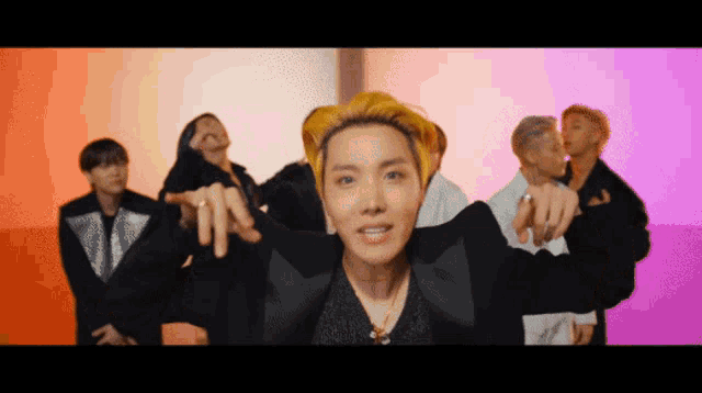 a group of people are dancing in front of a colorful background and one of them is pointing at the camera