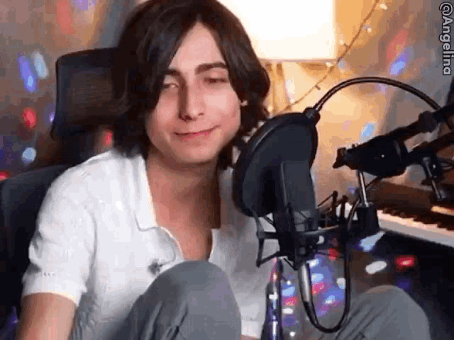 a young man is sitting in front of a microphone in a room with a piano .