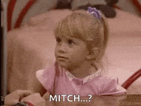 a little girl in a pink dress is sitting on a bed talking to a man .