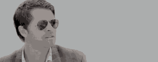 a man wearing sunglasses and a suit is looking at the camera .