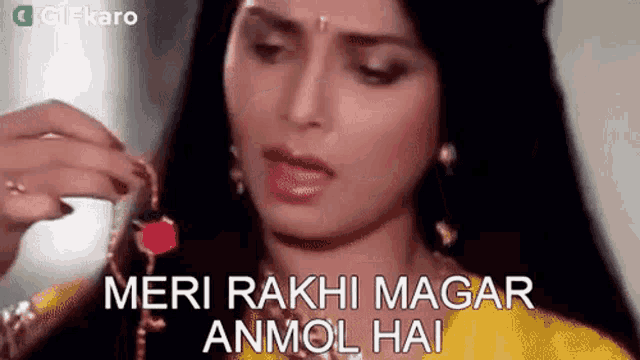 a woman in a yellow dress is holding a red flower in her hand and says `` meri raki magar anmol hai '' .