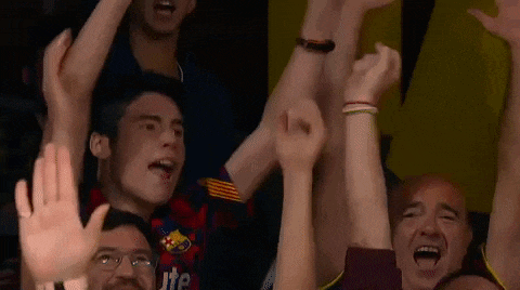 a group of people are sitting in a stadium raising their hands in the air .