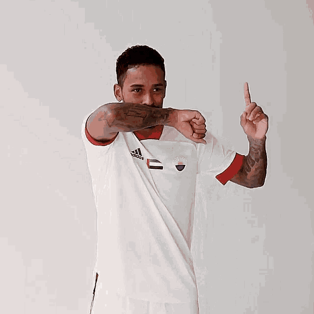 a man wearing a white adidas shirt is pointing upwards
