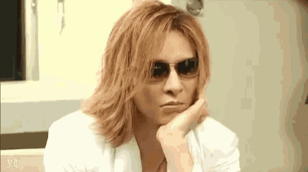 a man with long hair wearing sunglasses and a white jacket