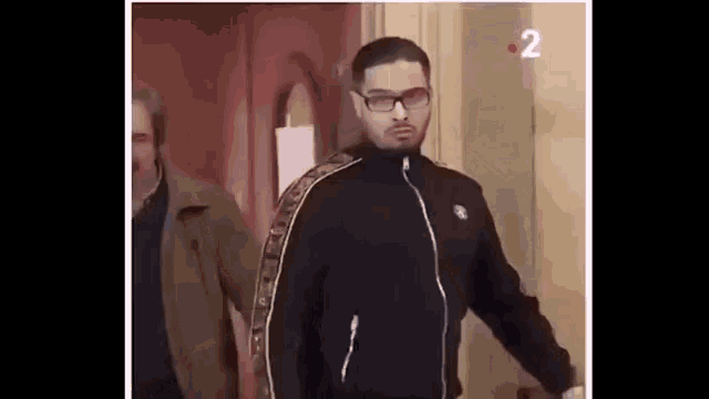 a man in a black jacket and glasses is walking through a doorway .
