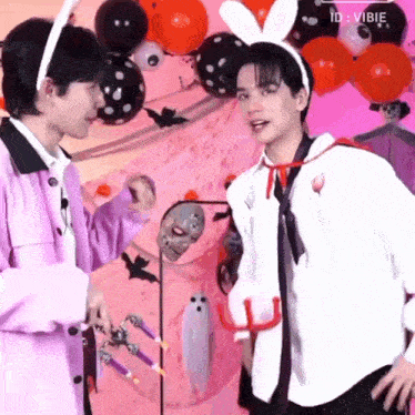 two men are standing next to each other in front of balloons and a ghost costume .