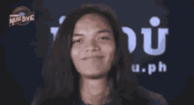 a man with long hair is smiling in front of a logo for music one
