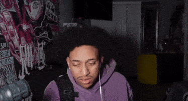 a man in a purple hoodie is sitting in front of a microphone .