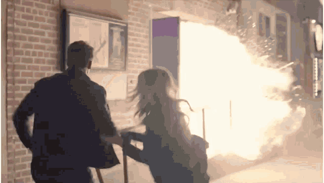 a man and a woman are standing in front of a building with a fire coming out of the door .