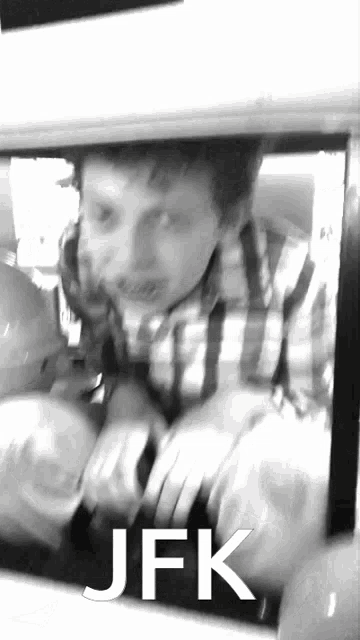 a man in a plaid shirt is looking out of a car window with jfk written on the bottom of the image