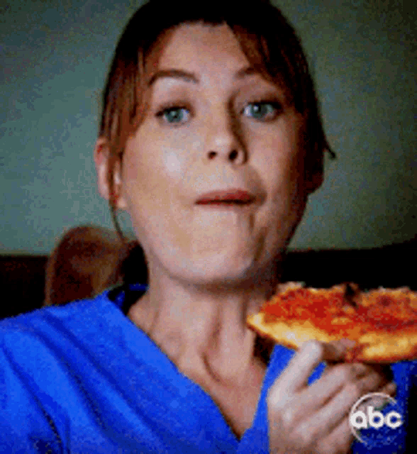 a woman in a blue scrub eating a slice of pizza