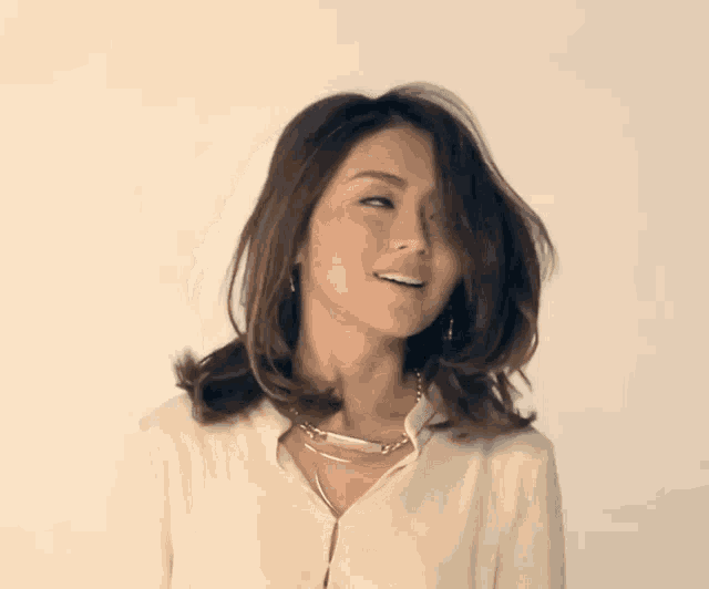 a woman wearing a white shirt and a gold necklace looks to the side