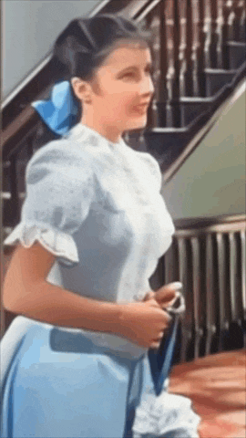 a woman in a blue dress stands in front of a staircase