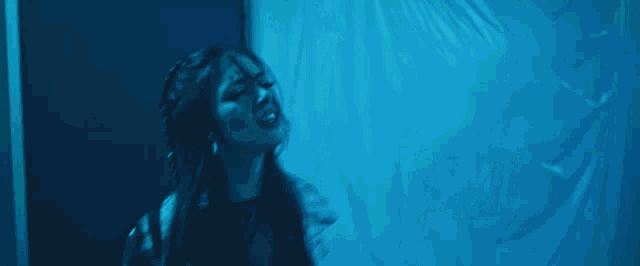 a woman stands in front of a man playing a guitar in a blue room