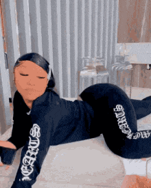a woman is laying on her stomach on the floor in a bathroom wearing a black hoodie and pants .