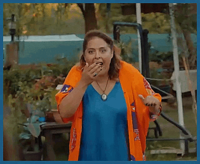 a woman wearing a blue shirt and an orange cardigan is smiling and waving .