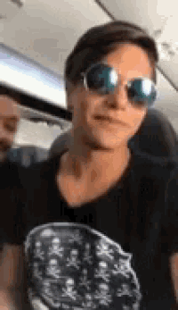 a man wearing sunglasses and a black shirt is sitting on a plane .