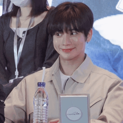 a young man is holding a bottle of water and a framed item that says cosmetique