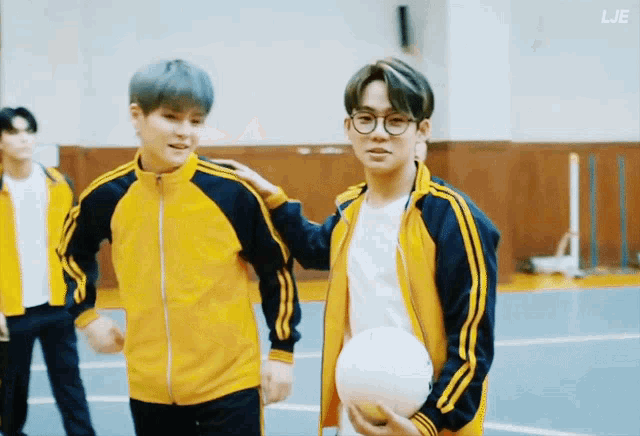 a man in a yellow jacket is standing next to another man holding a volleyball