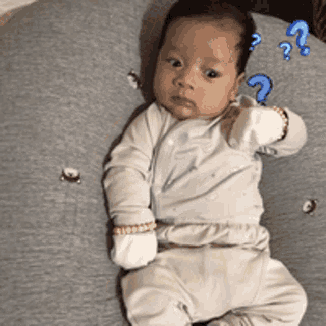 a baby is laying on a pillow with a question mark in the background