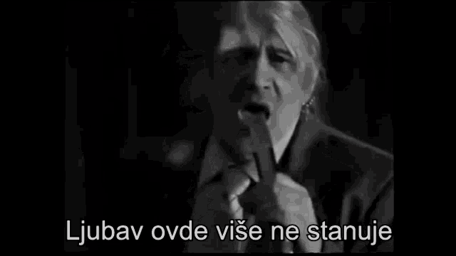 a man in a suit and tie singing into a microphone with the words ljubav ovde vise ne stanuje above him
