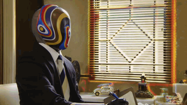 a man with a colorful mask on his head sits at a desk