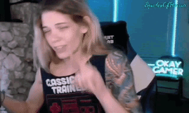 a woman is sitting in a chair in front of a computer screen wearing a black tank top that says okay gamer .
