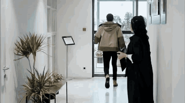 a man and a woman are walking through a hallway with a sign on the wall