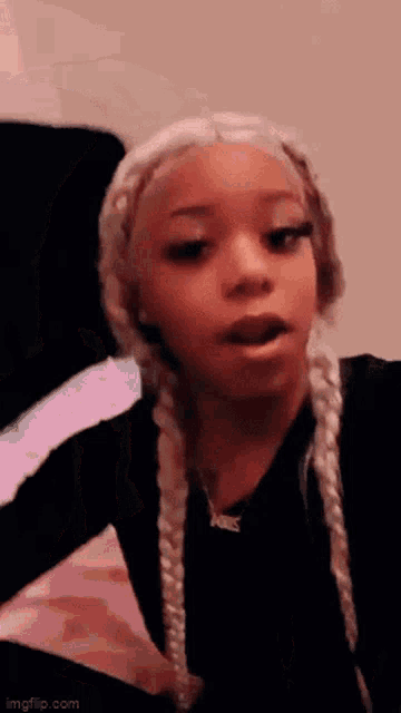 a young girl with blonde braids is making a funny face while sitting on a bed .