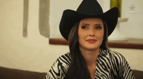 a woman wearing a cowboy hat and a zebra print shirt is sitting on a couch