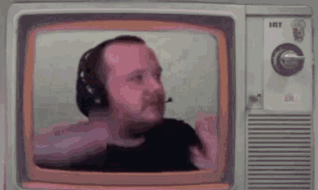 a man wearing headphones and a microphone is sitting in front of a television screen .