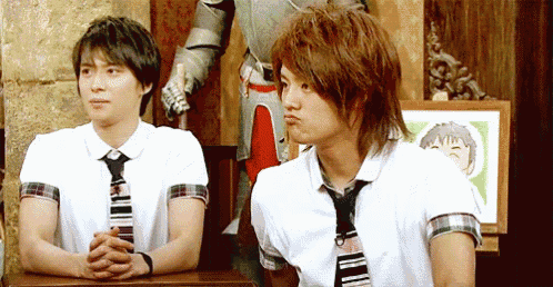 two young men are sitting at a table with their hands folded in front of a knight in armor