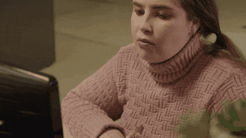 a woman in a pink sweater is sitting in front of a computer monitor