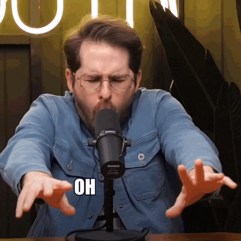 a man wearing glasses and a shure microphone is making a funny face
